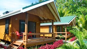 Une cabane en bois avec une terrasse, des chaises rouges et un jardin agrémenté de fleurs rouges.