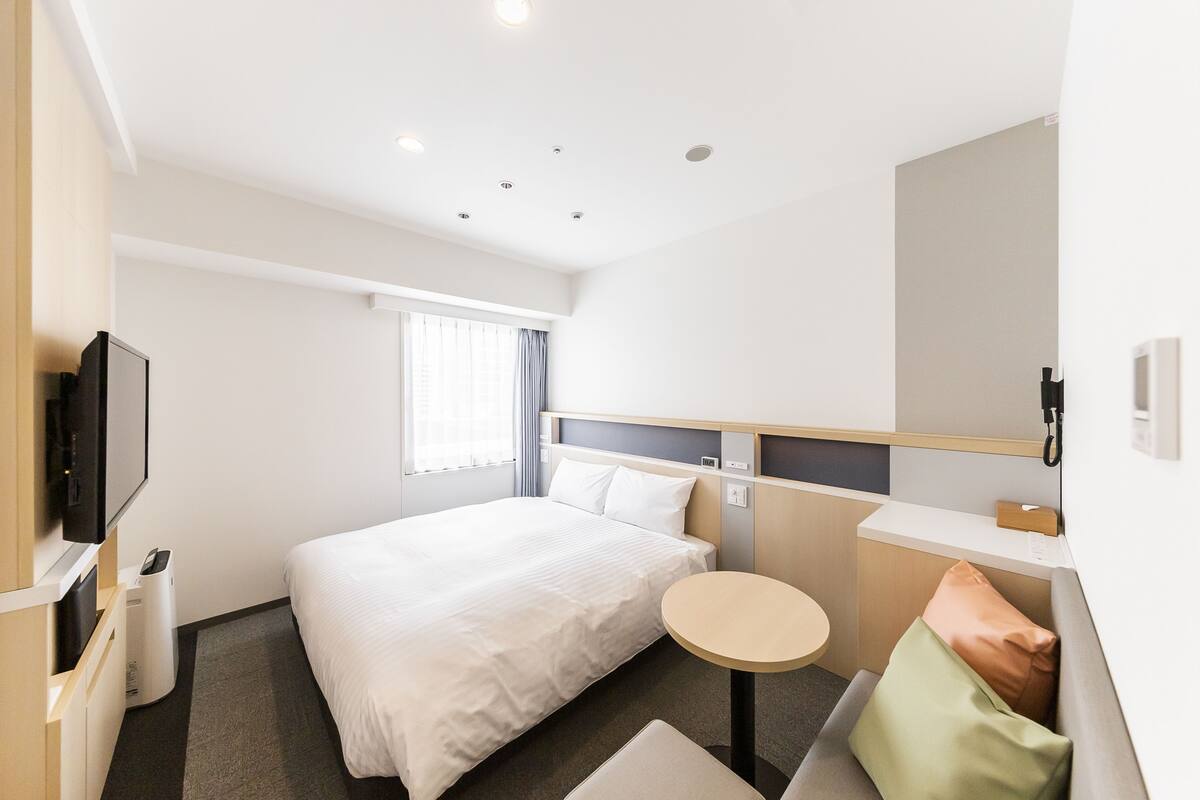 A hotel room with a bed, a round table, a TV, and a window with curtains.