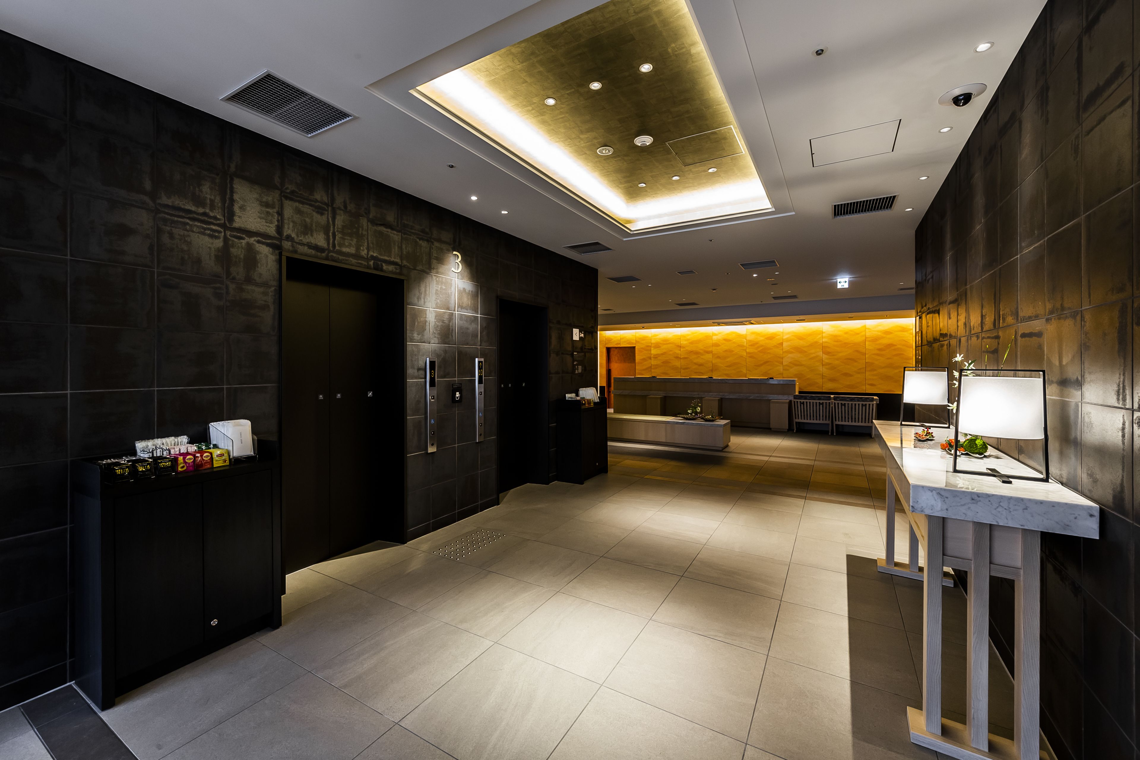 A modern hotel lobby with a reception desk, a seating area, and a large window.