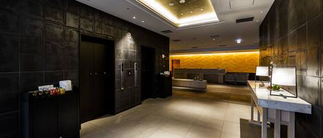 A modern hotel lobby with a reception desk, a seating area, and a large window.