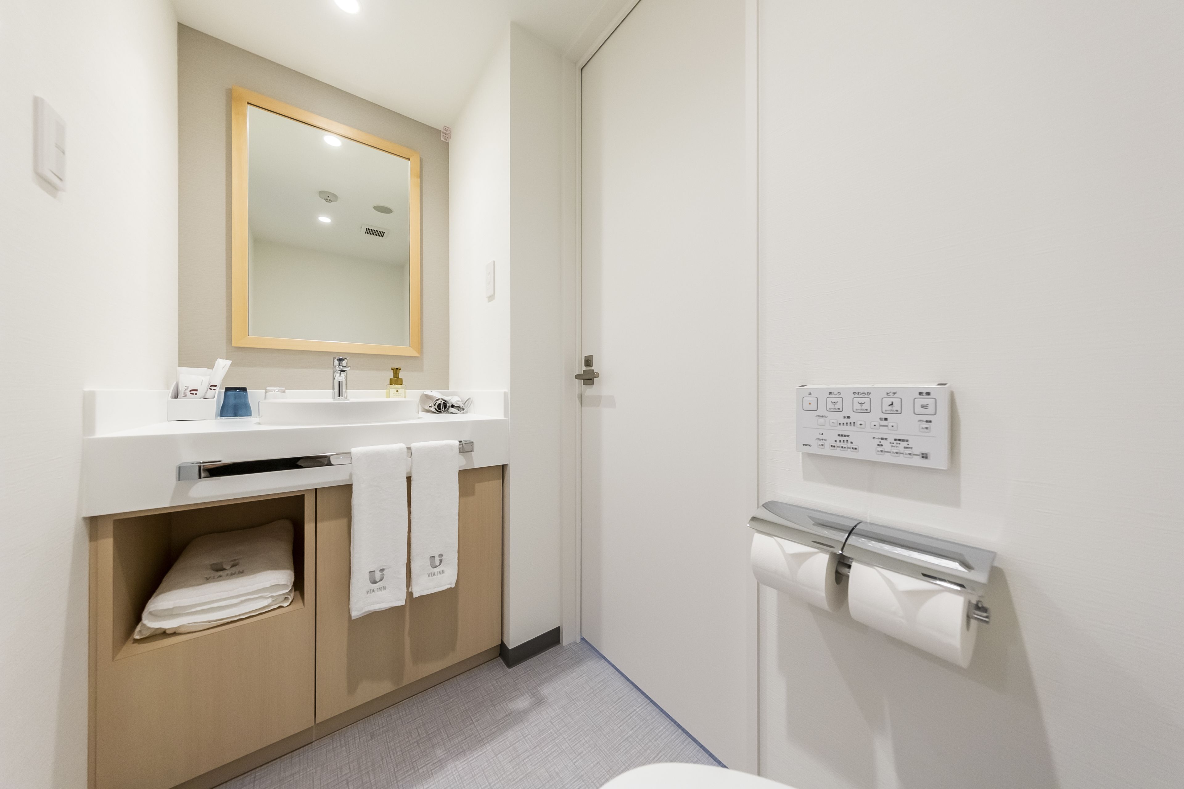 A modern bathroom with a sink, mirror, towel racks, and a toilet paper holder.
