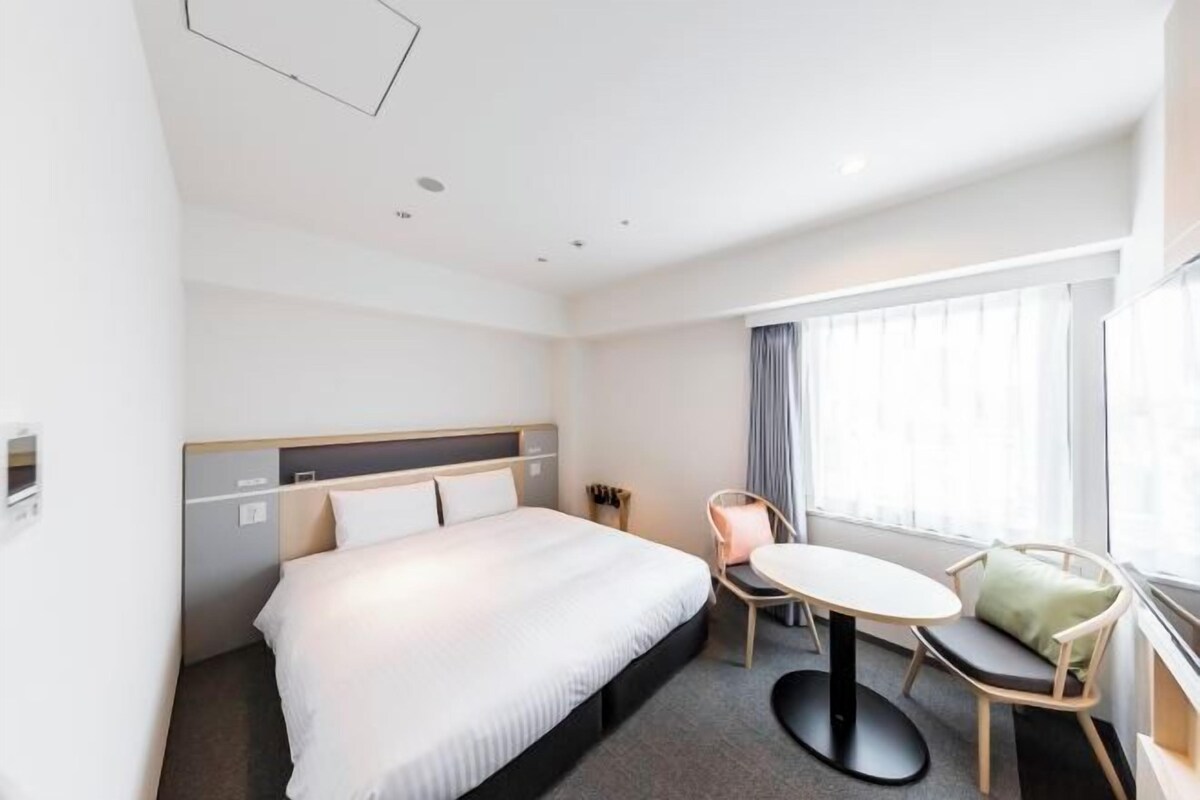 A hotel room with a bed, a round table, and a chair.