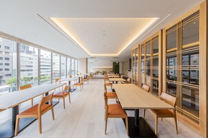 A modern conference room with long tables and chairs, large windows, and a view of the cityscape.