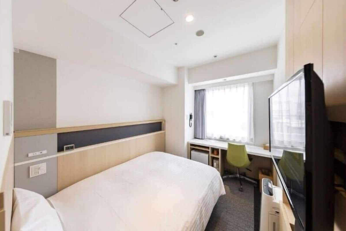A hotel room with a bed, desk, chair, TV, and a window with curtains.