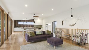 A modern living room with a sofa, ottoman, and patterned chairs, a kitchen in the background, and a dining area. - Clovelly (Lorne)