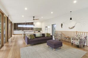 A modern living room with a sofa, ottoman, and patterned chairs, a kitchen in the background, and a dining area. - Clovelly (Lorne)