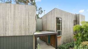 A modern building with a wooden exterior, a covered walkway, and a small garden area. - Clovelly (Lorne)