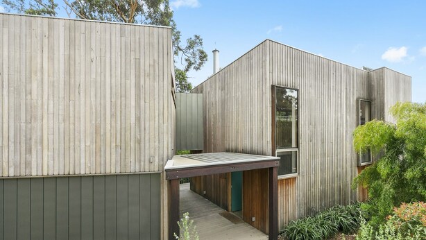 A modern building with a wooden exterior, a covered walkway, and a small garden area.