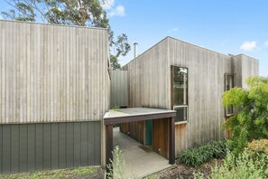 A modern building with a wooden exterior, a covered walkway, and a small garden area. - Clovelly (Lorne)