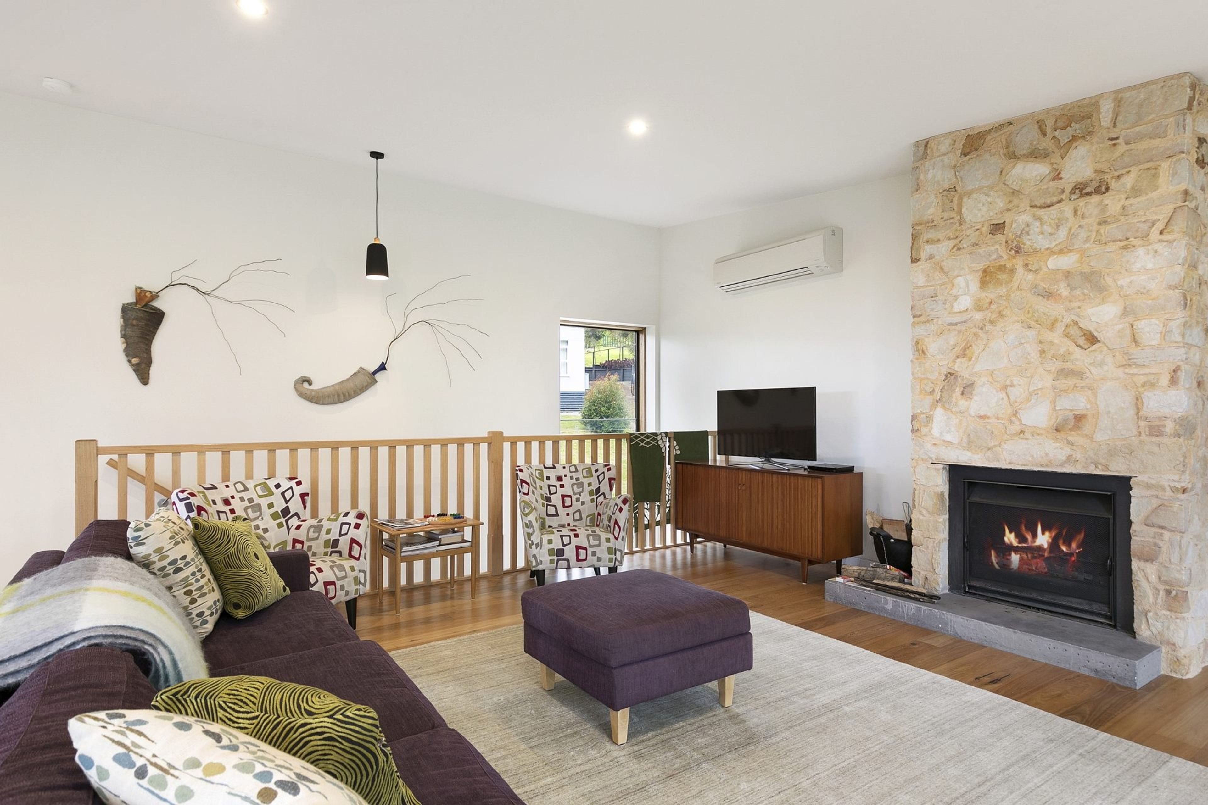A modern living room with a stone fireplace, a sofa with patterned cushions, a television, and a wooden railing.
