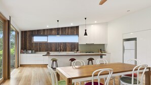 A modern kitchen with white cabinets, a wooden countertop, and a dining area with a wooden table and white chairs. - Clovelly (Lorne)