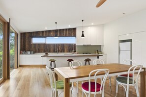 A modern kitchen with white cabinets, a wooden countertop, and a dining area with a wooden table and white chairs. - Clovelly (Lorne)