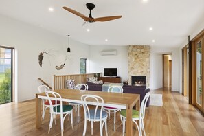 A modern living room with a dining area, a fireplace, and a ceiling fan.