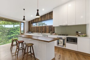 A modern kitchen with a large island, wooden accents, and a view of greenery.