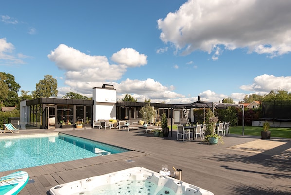 Un área de piscina con un jacuzzi, sillones de descanso y una zona de estar techada.
