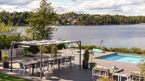 Zona junto a la piscina con una pérgola, asientos y vistas a un lago.