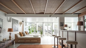 Una habitación de hotel moderna con una cama grande, una zona de estar con una mesa de centro y un área de bar con taburetes.