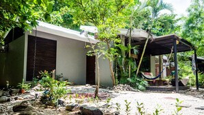 A modern house with a covered porch, surrounded by lush greenery and a garden with rocks and plants. - Las Avellanas Villas Costa Rica - Full equipped house(max 2p) (Santa Cruz)
