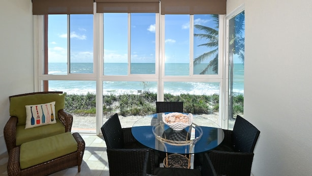A room with a glass table and chairs, a wicker armchair, and a view of the ocean through large windows. - Turtle Beach - Gulf-Front Condo - 2BR - Free Boat Docks - Siesta Key (Siesta Key)