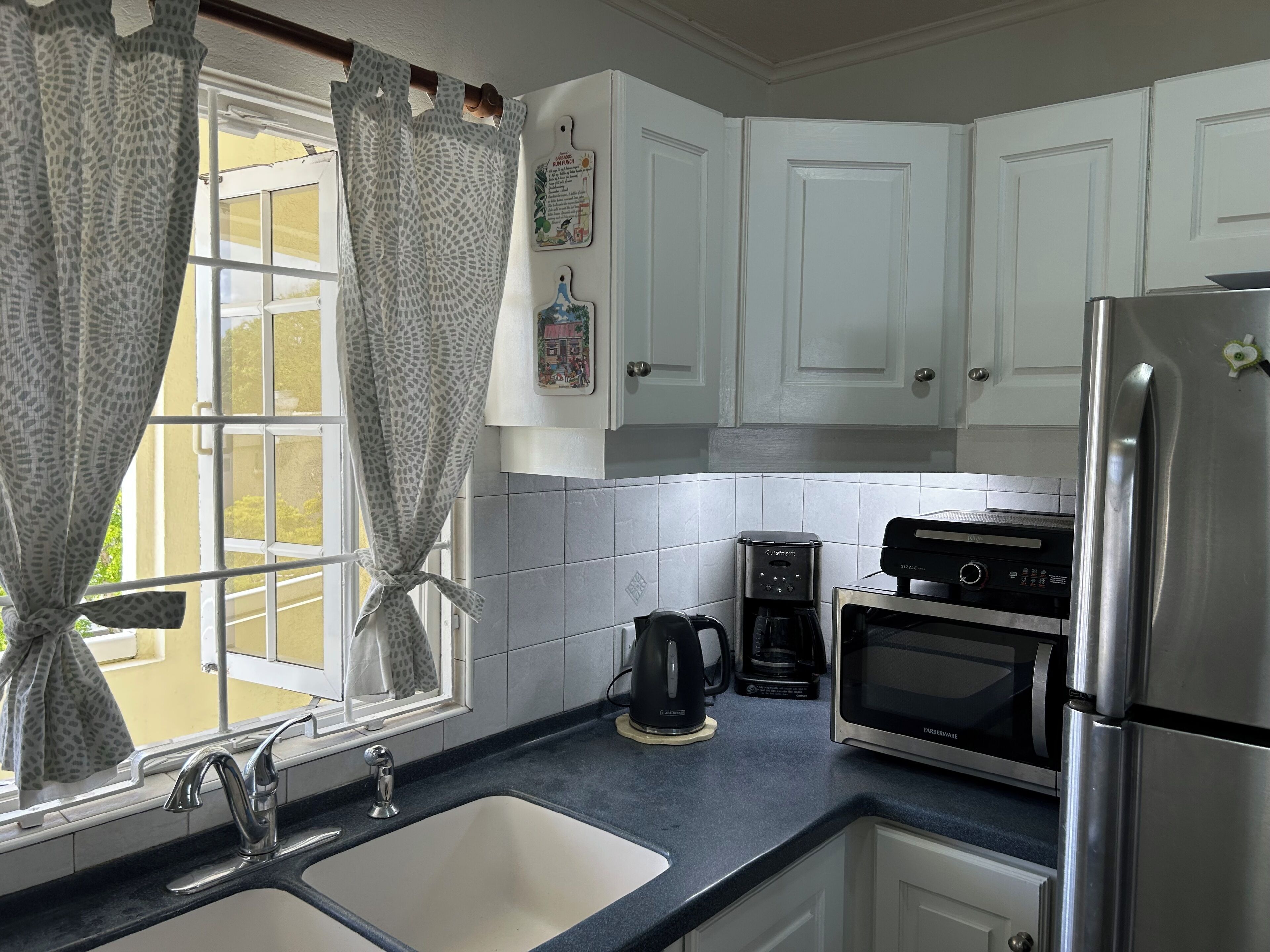 A kitchen with white cabinets, a stainless steel refrigerator, a coffee maker, and a microwave.