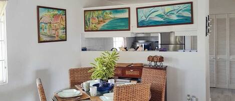 A dining area with wicker chairs, a round table, and a ceiling fan. There are three framed paintings on the wall above the table.