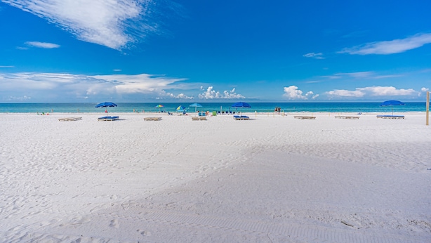 En strand med vit sand, klarblå himmel och ett lugnt hav.