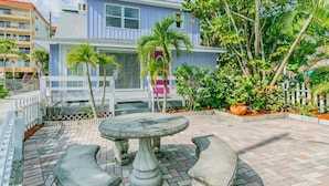 A two-story building with a balcony, a stone table, and a white picket fence. - Studio by the Sand  & Johns Pass (Madeira Beach)