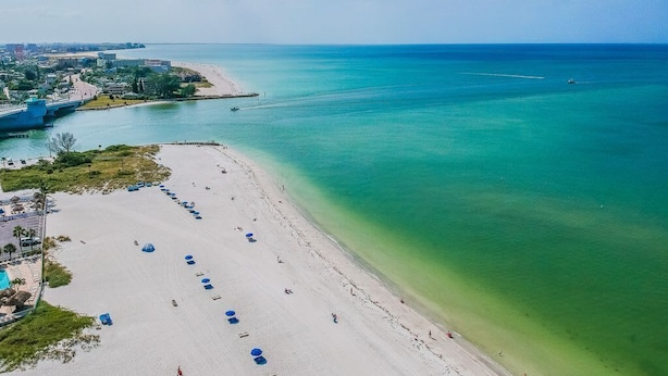 A beach with a clear view of the ocean, a bridge, and a cityscape in the background. - Studio by the Sand  & Johns Pass (Madeira Beach)