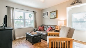 A living room with a leather sofa, wooden armchair, and ottoman, a television on a cabinet, and a ceiling fan. - Studio by the Sand  & Johns Pass (Madeira Beach)