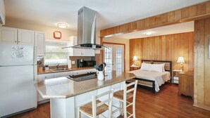 A modern kitchen with a central island, a dining area with a table and chairs, and a bedroom with a bed and bedside tables. - Studio by the Sand  & Johns Pass (Madeira Beach)