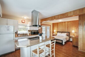 A modern kitchen with a central island, a dining area with a table and chairs, and a bedroom with a bed and bedside tables. - Studio by the Sand  & Johns Pass (Madeira Beach)