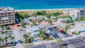 An aerial view of a coastal area with buildings, a parking lot, and a beach. - Studio by the Sand  & Johns Pass (Madeira Beach)