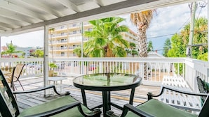 A covered outdoor seating area with a glass table and chairs, overlooking a residential building and palm trees. - Studio by the Sand  & Johns Pass (Madeira Beach)