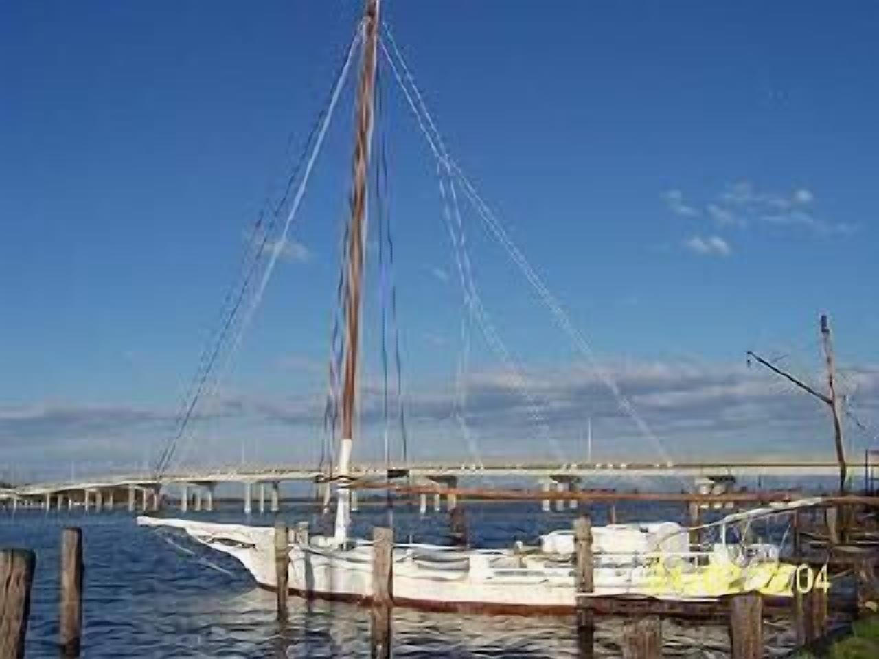 Un puerto deportivo con barcos amarrados, un puente al fondo y un cielo despejado.
