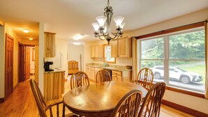 A spacious kitchen with wooden cabinets, a dining table, and chairs. There is a large window with a view of the outside. - Pet Friendly Red House: Short Walk to Private Dock & Lake George!  (Lake George)
