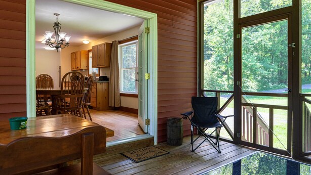 A wooden interior with a dining area, a chandelier, and a view through large windows. - Pet Friendly Red House: Short Walk to Private Dock & Lake George!  (Lake George)