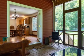 Un intérieur en bois comprenant un coin repas, un lustre et une vue dégagée sur l’extérieur grâce à de grandes fenêtres.