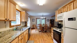 A kitchen with wooden cabinets, a granite countertop, a dining table with chairs, a microwave, a stove, and a refrigerator. - Pet Friendly Red House: Short Walk to Private Dock & Lake George!  (Lake George)