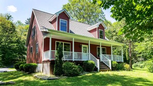 A two-story house with a front porch, a covered entryway, and a steeply pitched roof. - Pet Friendly Red House: Short Walk to Private Dock & Lake George!  (Lake George)