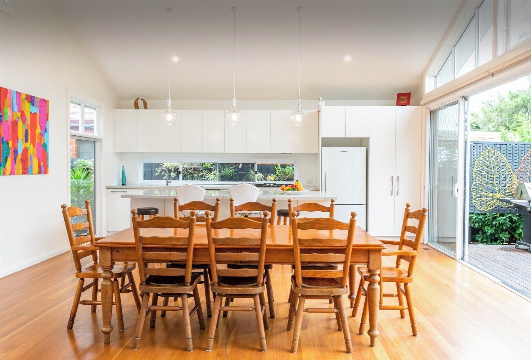 A modern kitchen with white cabinets, a central island, and a dining area with wooden chairs and a table.
