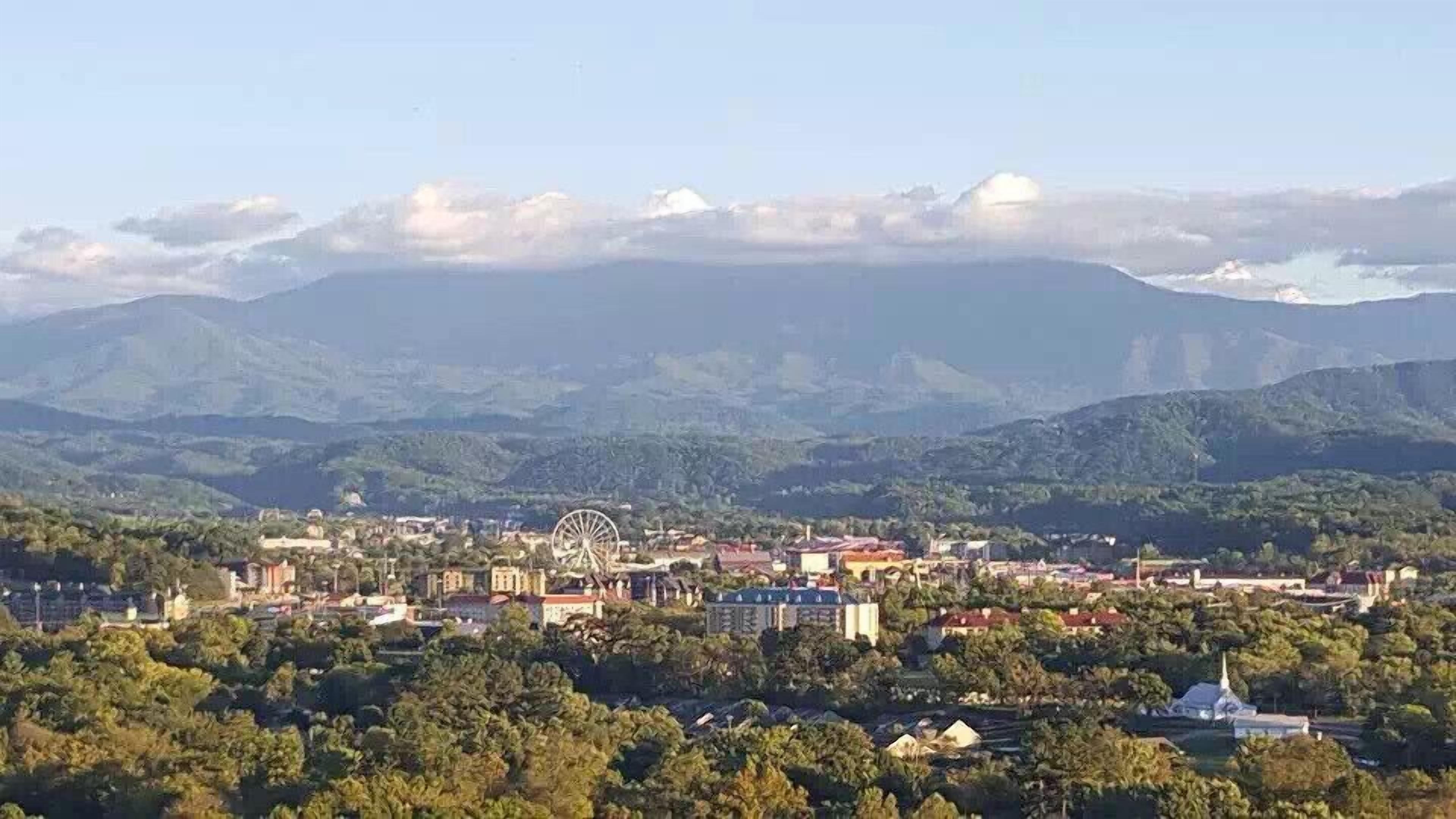 A town with a prominent Ferris wheel, surrounded by lush green hills and mountains.