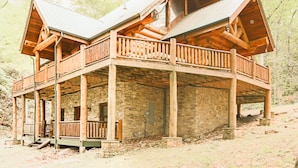 Una cabaña de troncos con cimientos de piedra, balcones de madera y techo de metal.