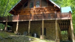 Una cabaña de troncos con balcón, rodeada de árboles.