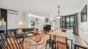 Una sala de estar moderna con un sofá, una mesa de centro y una televisión. Hay un comedor con una mesa y sillas de madera.