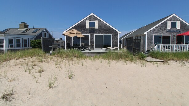 A beachfront property with multiple houses, a sandy beach, and a grassy area.