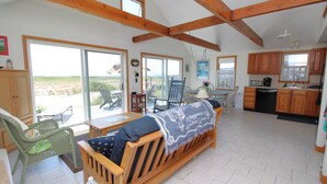 A spacious living area with a sofa, dining table, and chairs, large windows, and a kitchen area.
