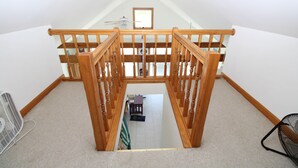 A wooden staircase with a ceiling fan, carpeted floor, and a small table with a chair.
