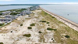 An aerial view of a coastal area with a row of houses along the beach and a sandy path leading to the water.