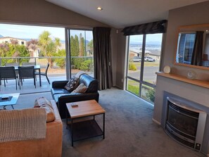 A spacious living room with a fireplace, a sofa, a coffee table, and a balcony with a view of the surrounding landscape.