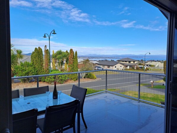 A balcony with a table and chairs, a clear view of the street and houses, and a metal railing.
